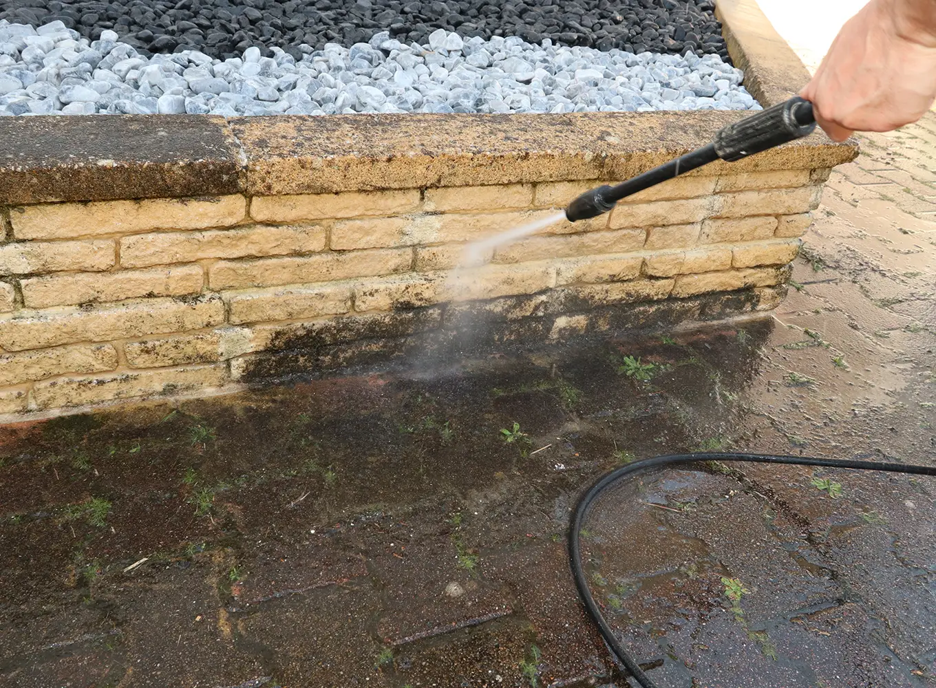 Person using a power washer to remove dirt from the side of a brick retaining wall in Grafton IL.